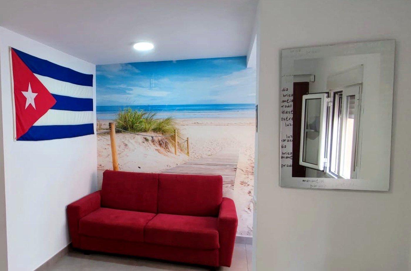 Salón de El Rinconcito Cubano en la Playa con sofá rojo, bandera cubana y mural de playa