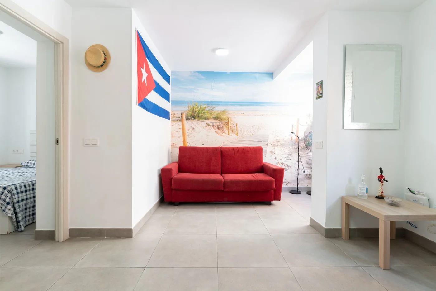 Salón de El Rinconcito Cubano en la Playa con sofá rojo, bandera cubana y mural de playa